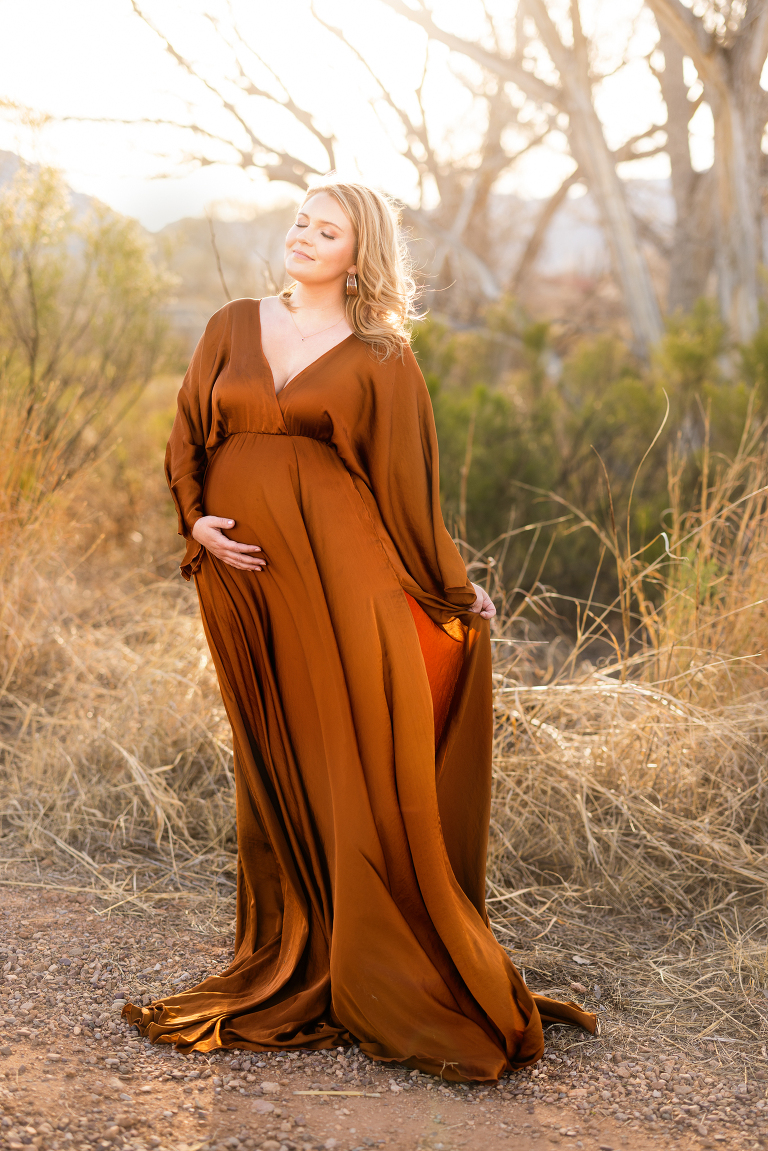 Pregnant woman in a gold dress getting photo taken for maternity session.