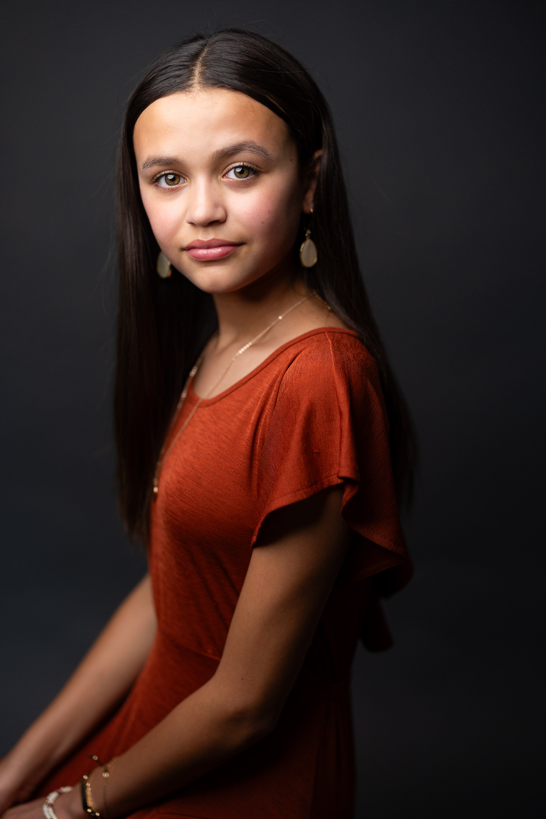 Young girl in an orange dress with a black background in a portrait studio.