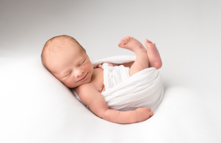 Sweet baby sleeping and smiling for newborn photos on a white backdrop.